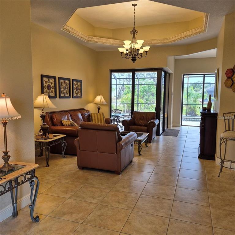 A living room with leather furniture, tile flooring, a tray ceiling, and sliding glass doors — 19 MEDALIST WAY, ROTONDA WEST, FL