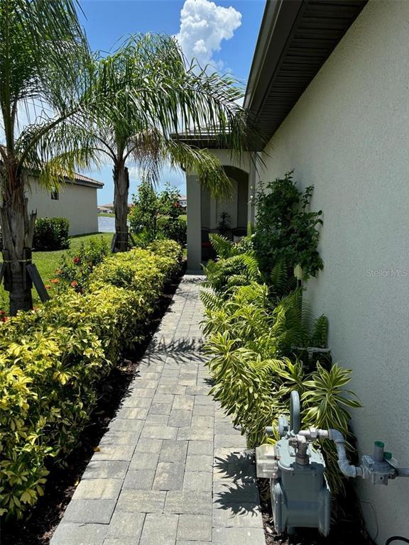 A paved walkway leads alongside a house exterior with lush landscaping and a gas meter — 5410 MYSTIC WATER COVE, BRADENTON, FL