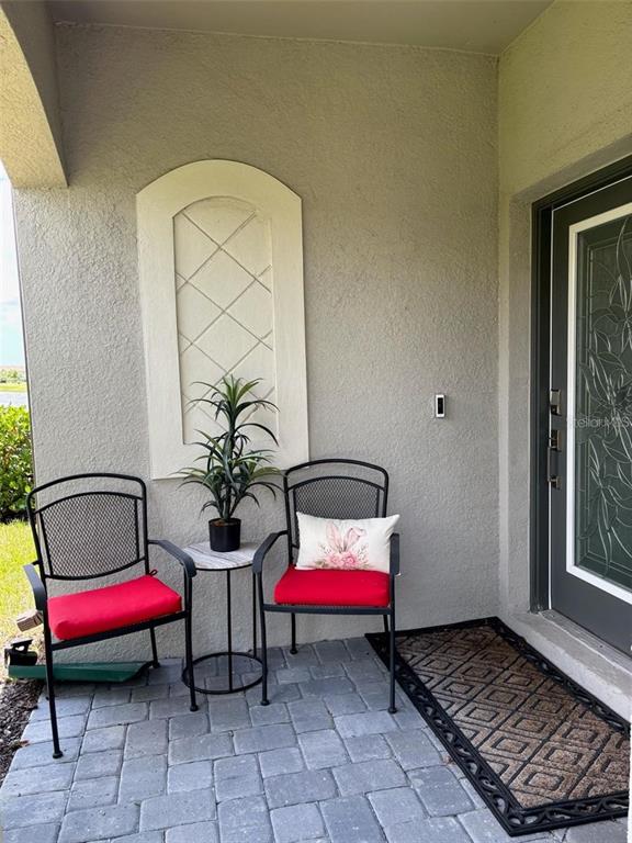 A covered entryway features two chairs with red cushions, a small table, and a door — 5410 MYSTIC WATER COVE, BRADENTON, FL