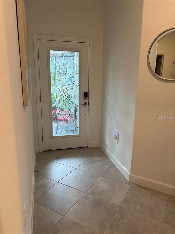An entryway features a white door with decorative glass, tile flooring, and a round mirror — 5410 MYSTIC WATER COVE, BRADENTON, FL