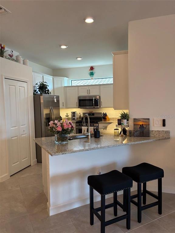 A kitchen features white cabinets, stainless steel appliances, granite countertops, and a breakfast bar — 5410 MYSTIC WATER COVE, BRADENTON, FL