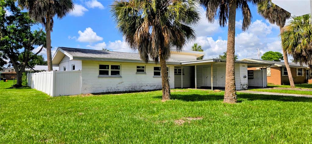 A white single-story house features a carport and palm trees under a blue sky — 204 BOBBIE CIRCLE, LAKELAND, FL