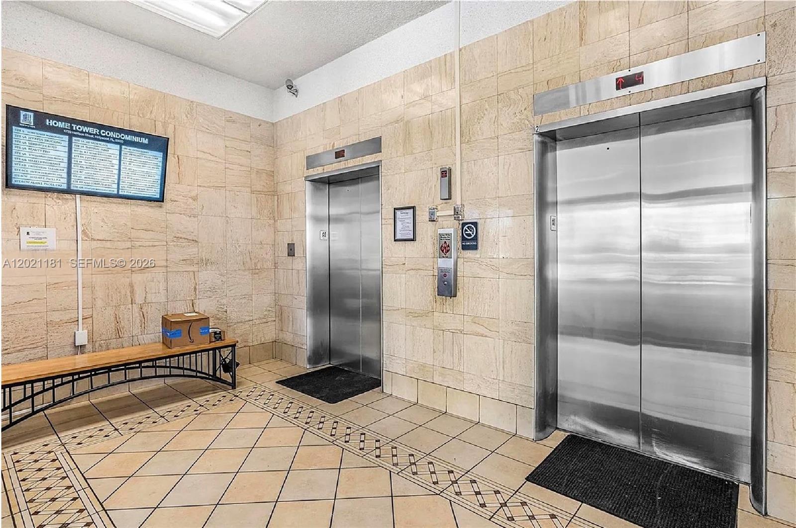A lobby features two stainless steel elevators, beige tiled walls, and a wooden bench — 1720 Harrison St # 5A, Hollywood FL 33020, HOLLYWOOD, FL