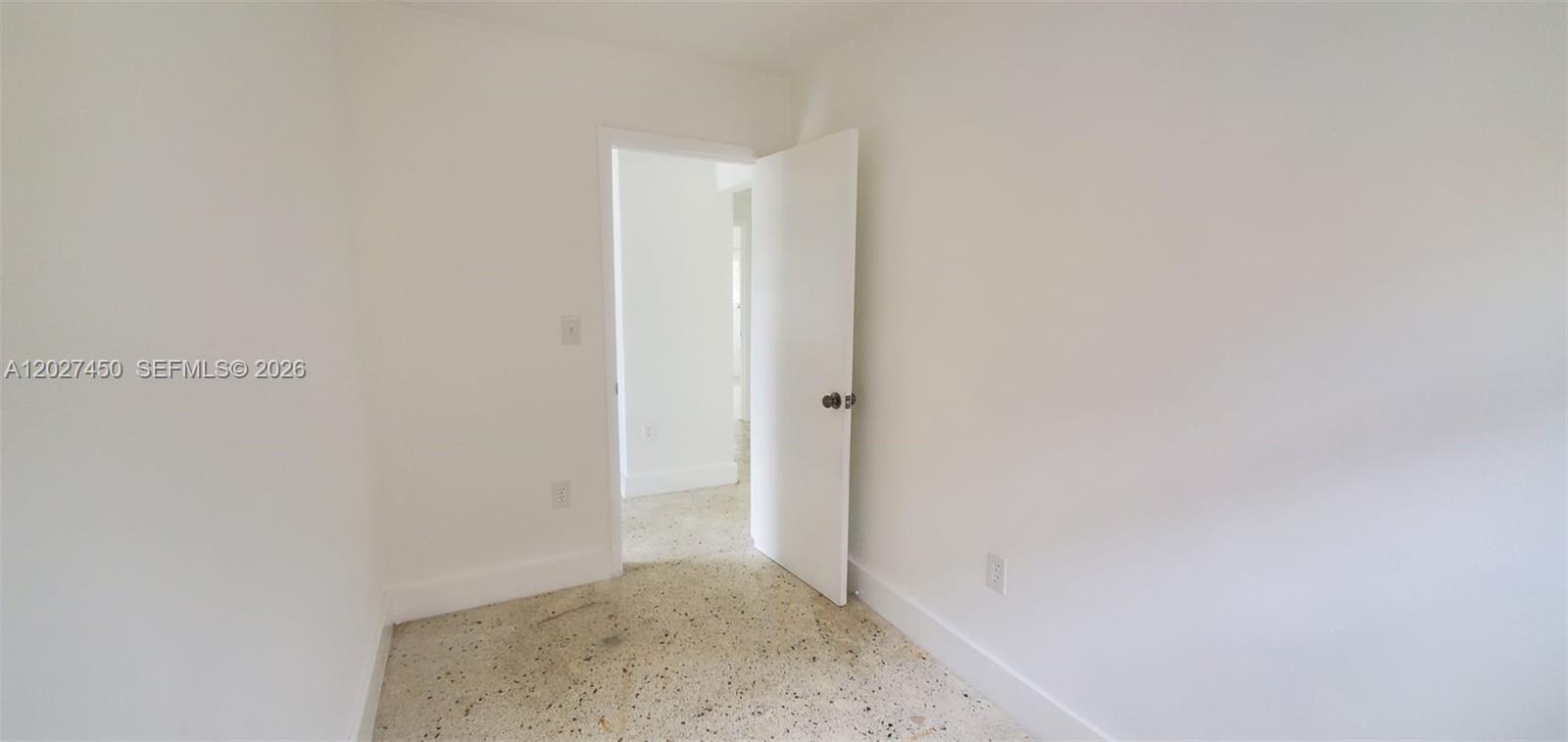 An empty room features white walls, a white door, and light-colored speckled flooring — 1032 SW 10th St, Miami FL 33130, MIAMI, FL
