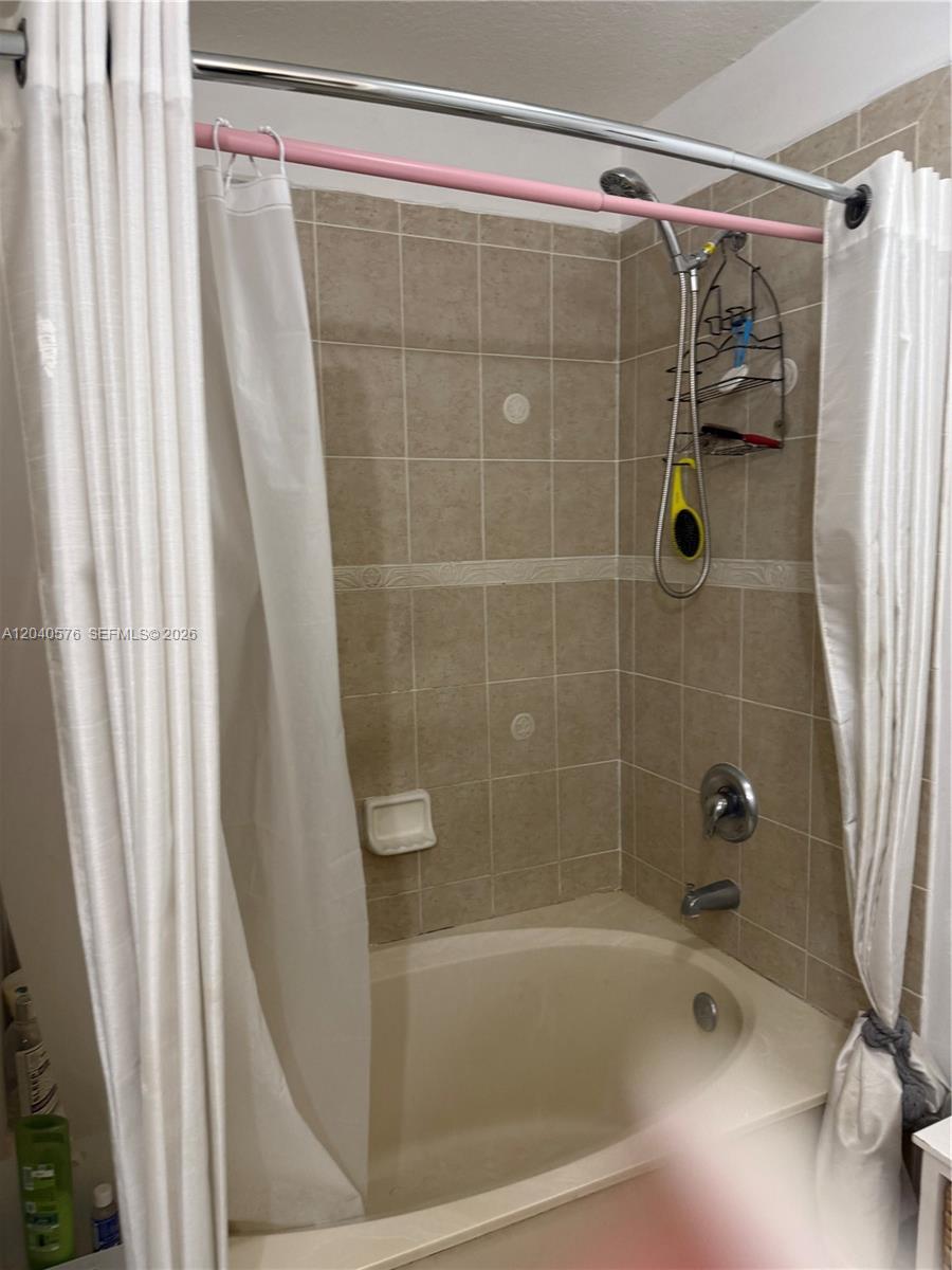 A bathtub with a shower head and beige tiled walls is enclosed by white curtains — 5943 SW 162nd Pl, Miami FL 33193, MIAMI, FL