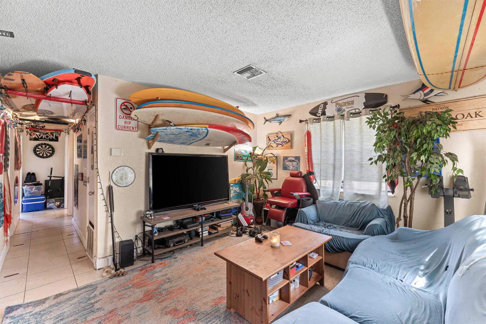 A living room decorated with surfboards, a television, a coffee table, and blue-covered sofas — 1717 NE 3rd Avenue, Delray Beach FL 33444, DELRAY BEACH, FL