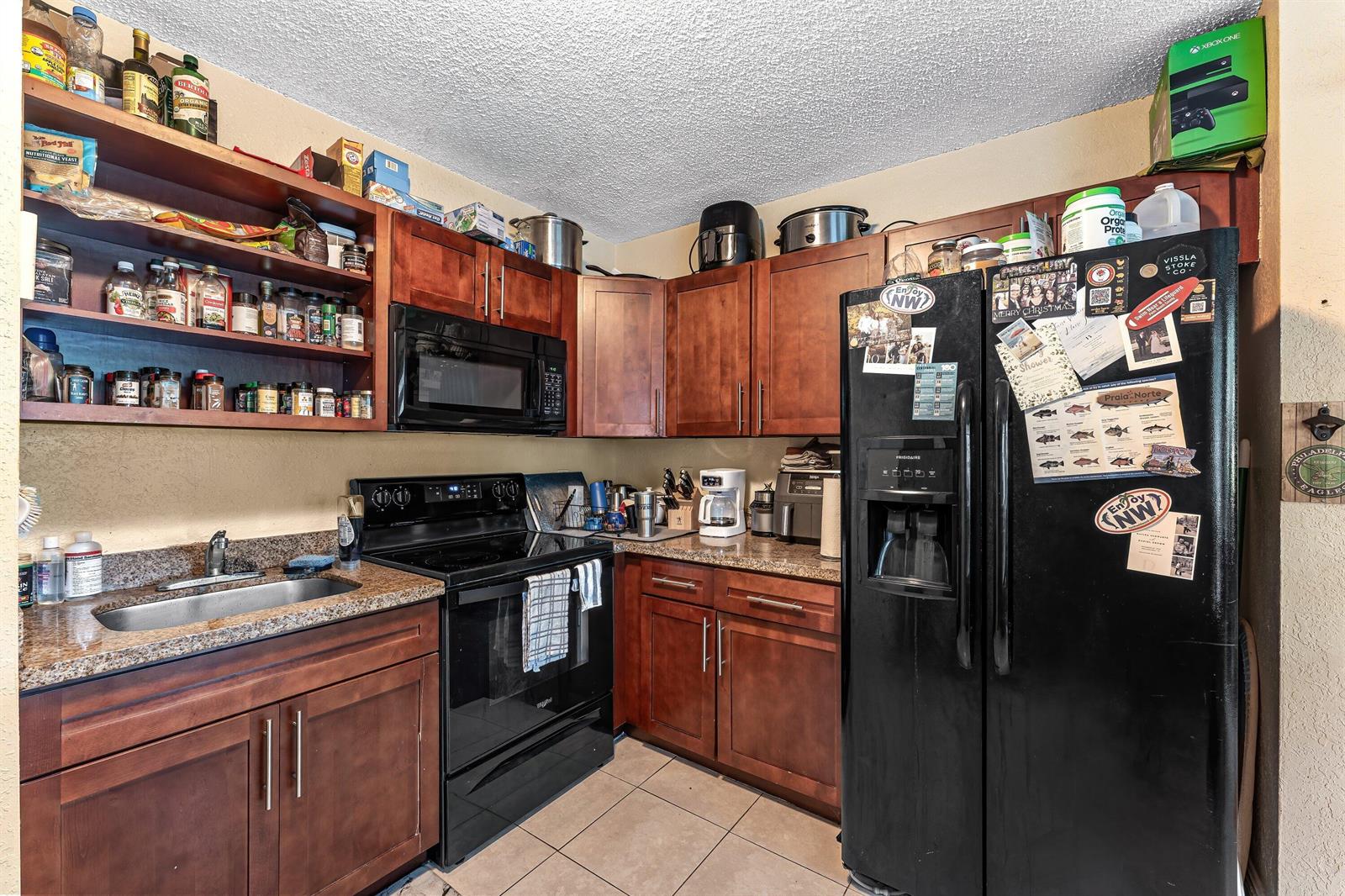 A kitchen features dark wood cabinets, black appliances, granite countertops, and open shelving — 1717 NE 3rd Avenue, Delray Beach FL 33444, DELRAY BEACH, FL