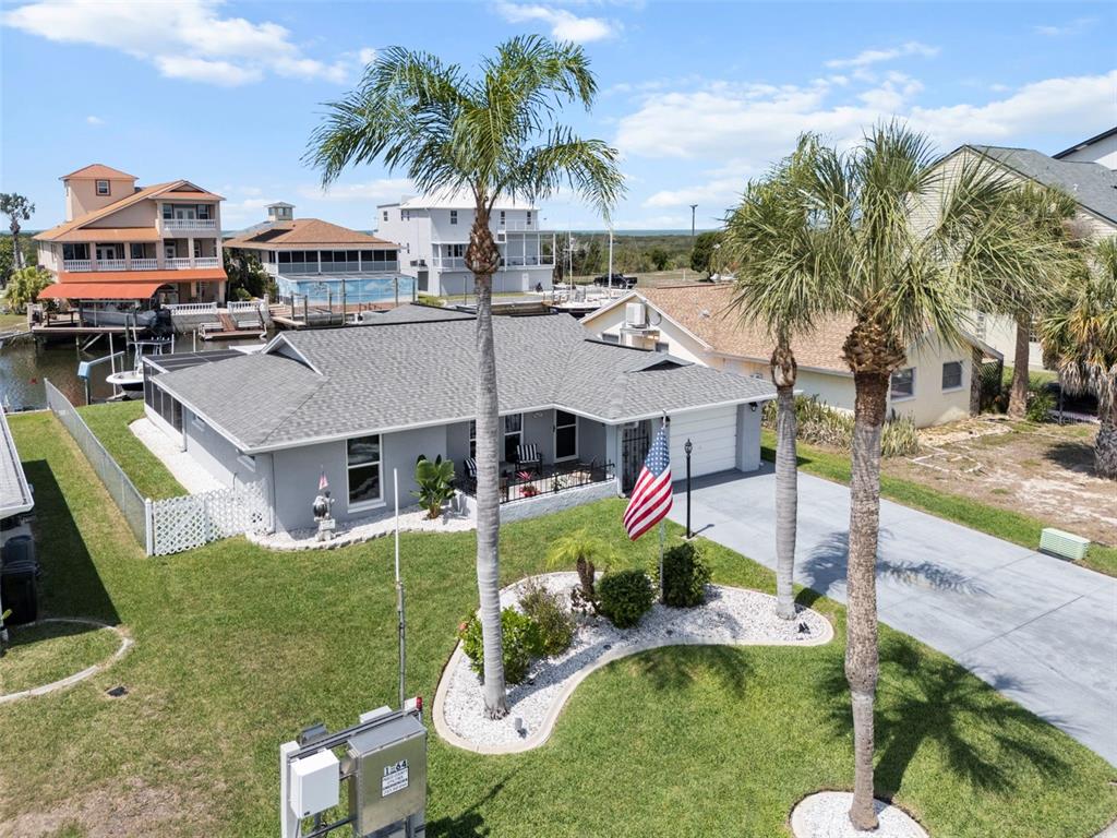 An aerial view shows a gray single-story house with a lawn, palm trees, and flag — 15627 DONZI DRIVE, HUDSON, FL