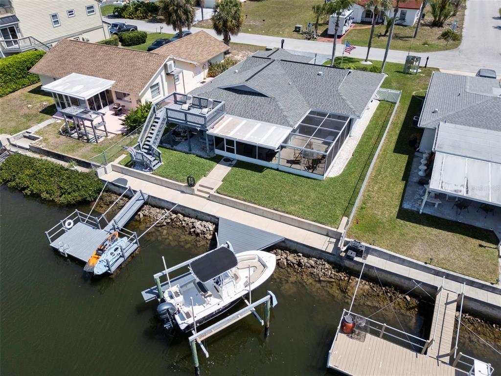 An aerial view shows a waterfront house with a boat dock, deck, and screened patio — 15627 DONZI DRIVE, HUDSON, FL
