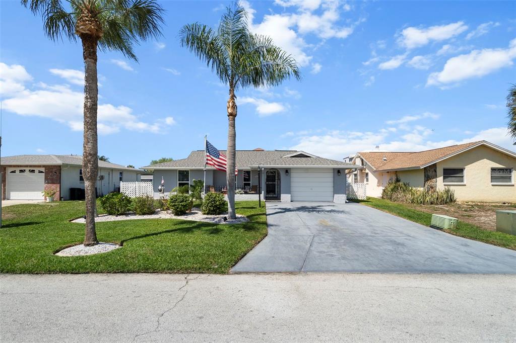 A single-story house with a gray exterior, a concrete driveway, and two palm trees — 15627 DONZI DRIVE, HUDSON, FL