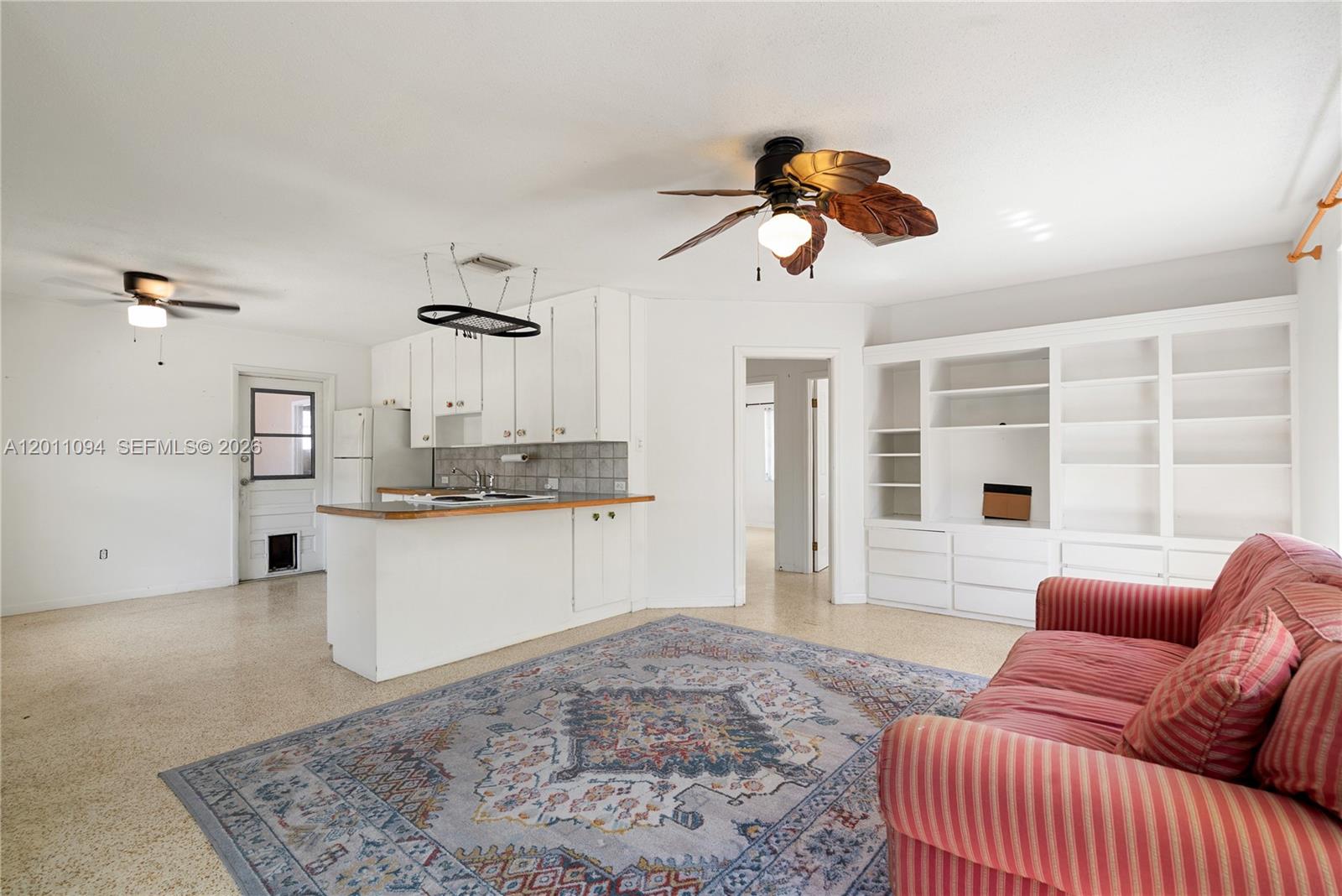 An open-concept living area features a kitchen with white cabinets, a ceiling fan, and built-in shelving — 56 SE Marlin Ave, Key Largo FL 33037, KEY LARGO, FL