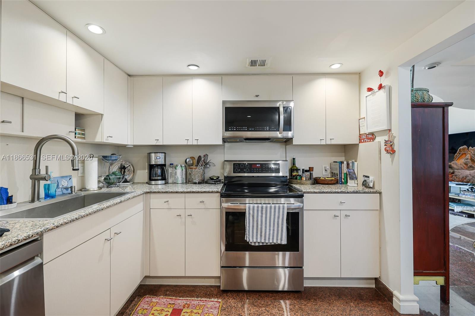 A kitchen features white cabinets, stainless steel appliances, granite countertops, and a brown tiled floor — 2 Grove Isle Dr # B1603, Miami FL 33133, MIAMI, FL