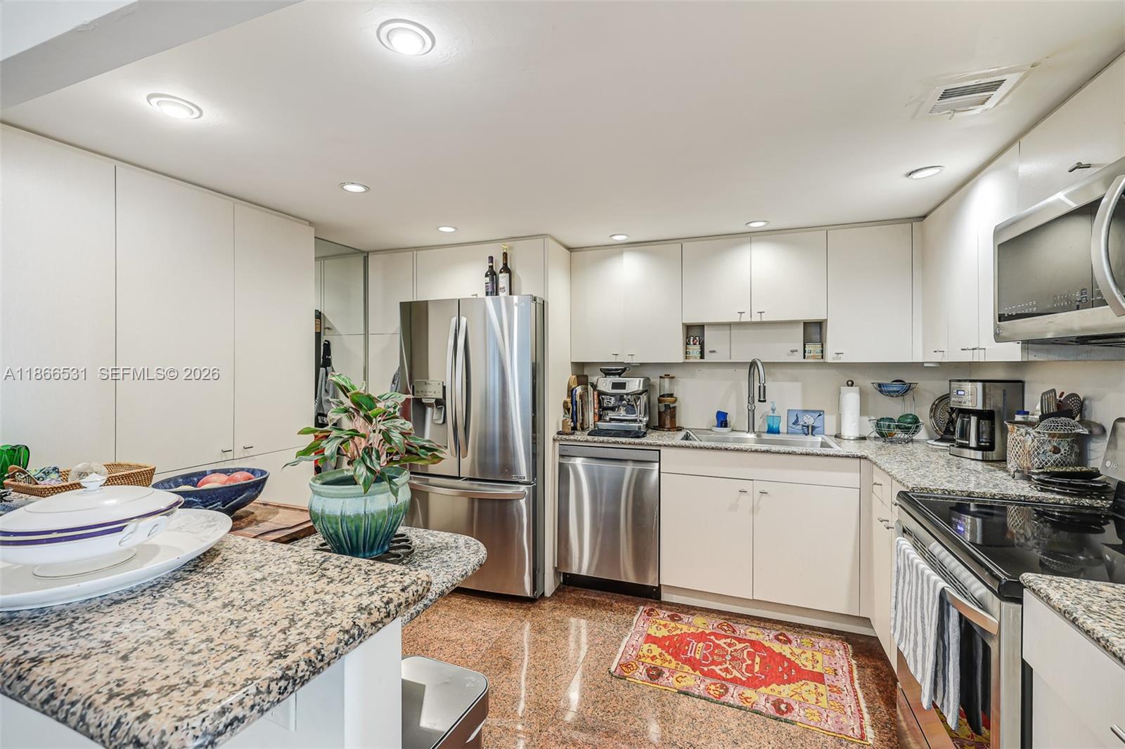 A kitchen features light-colored cabinetry, stainless steel appliances, granite countertops, and a patterned area rug — 2 Grove Isle Dr # B1603, Miami FL 33133, MIAMI, FL
