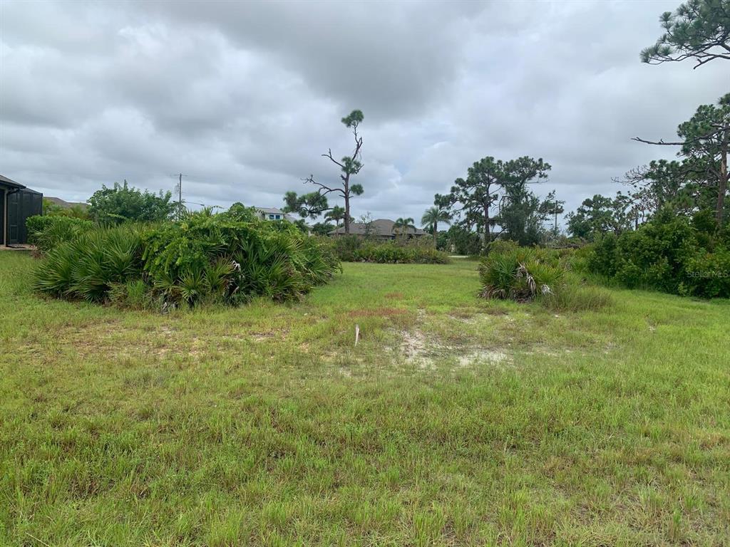 A vacant, grassy residential lot features scattered shrubs and trees under a cloudy sky — 6 AFT COURT, PLACIDA, FL