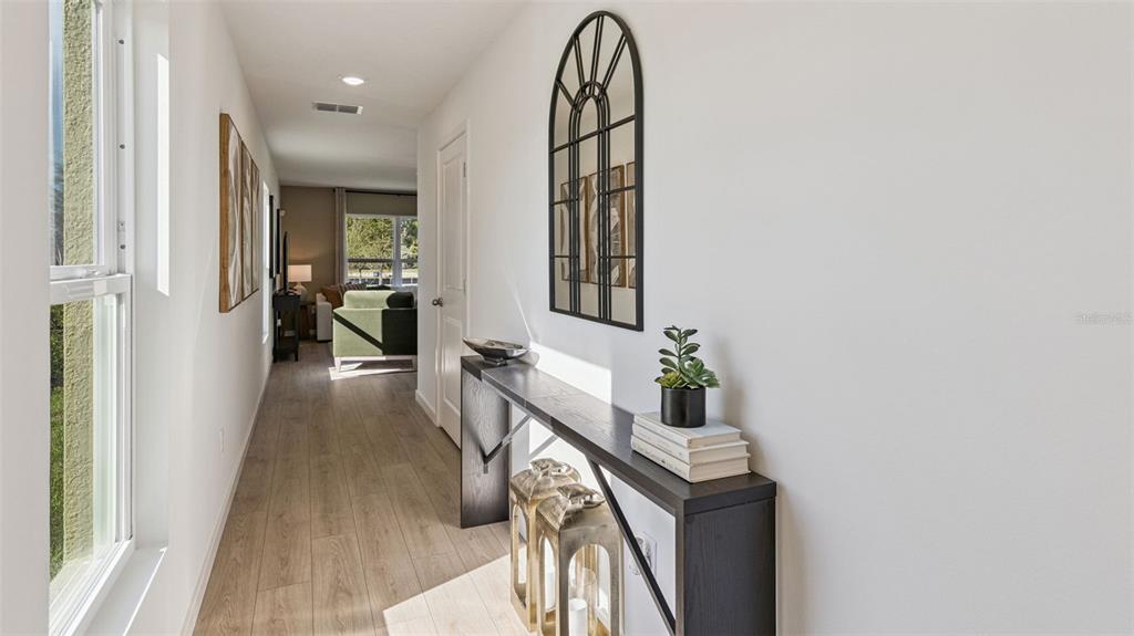A hallway with light wood flooring leads to a living area featuring a console table — 550 REMICK STREET, OSTEEN, FL