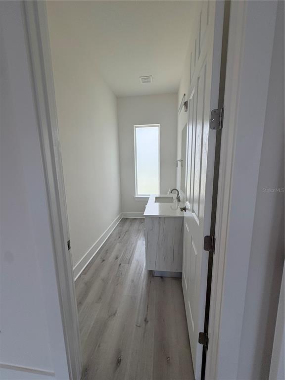 A narrow bathroom features a white vanity, light wood-look flooring, and a single window — 15384 HENNIPEN CIRCLE, PORT CHARLOTTE, FL