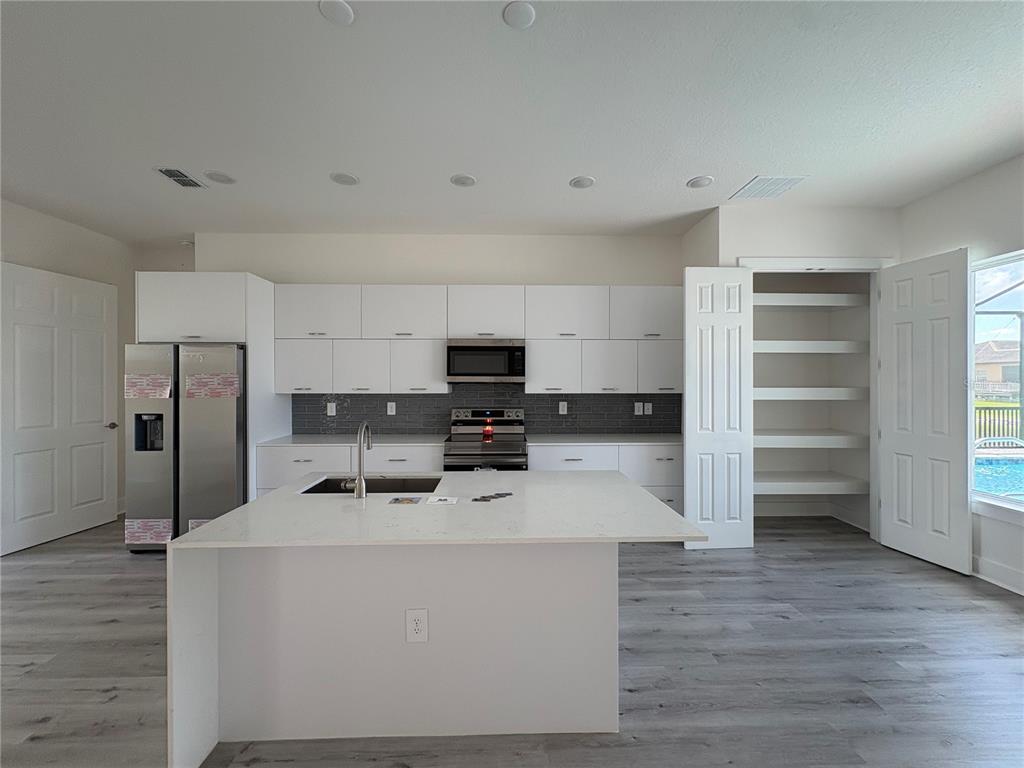 A modern kitchen features white cabinetry, a large island, stainless steel appliances, and a pantry — 15384 HENNIPEN CIRCLE, PORT CHARLOTTE, FL