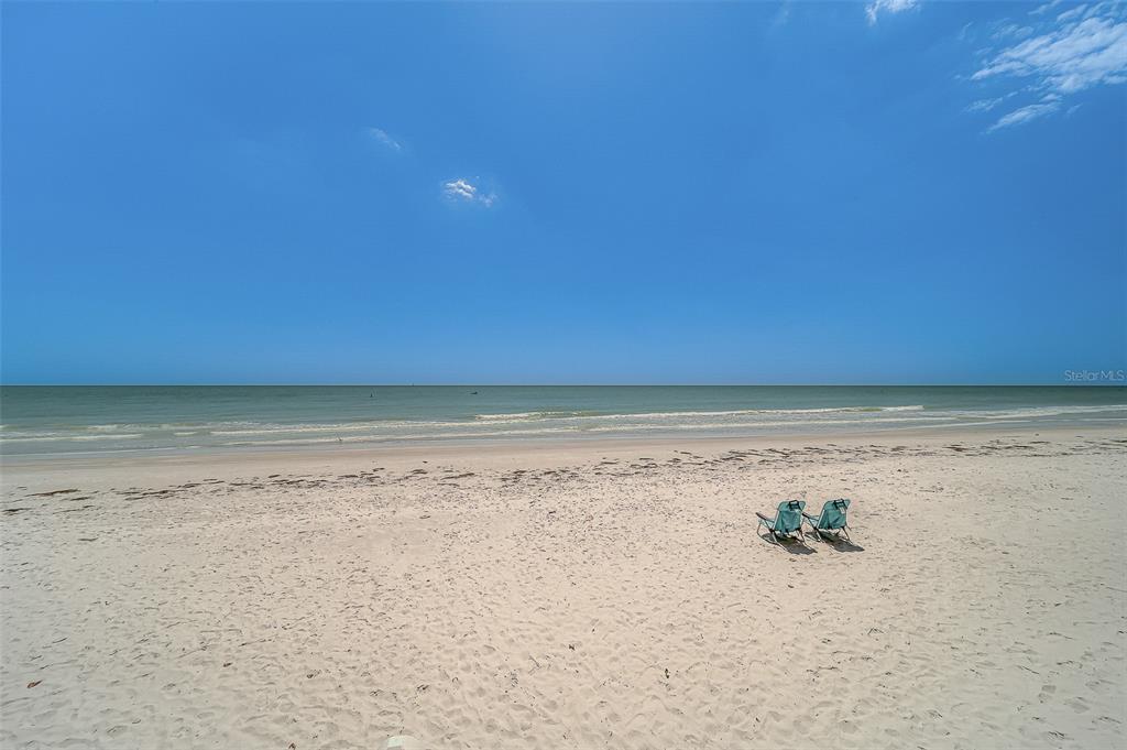 A covered balcony with wicker lounge chairs overlooks a sandy beach and the ocean — 16450 GULF BOULEVARD UNIT 565, NORTH REDINGTON BEACH, FL