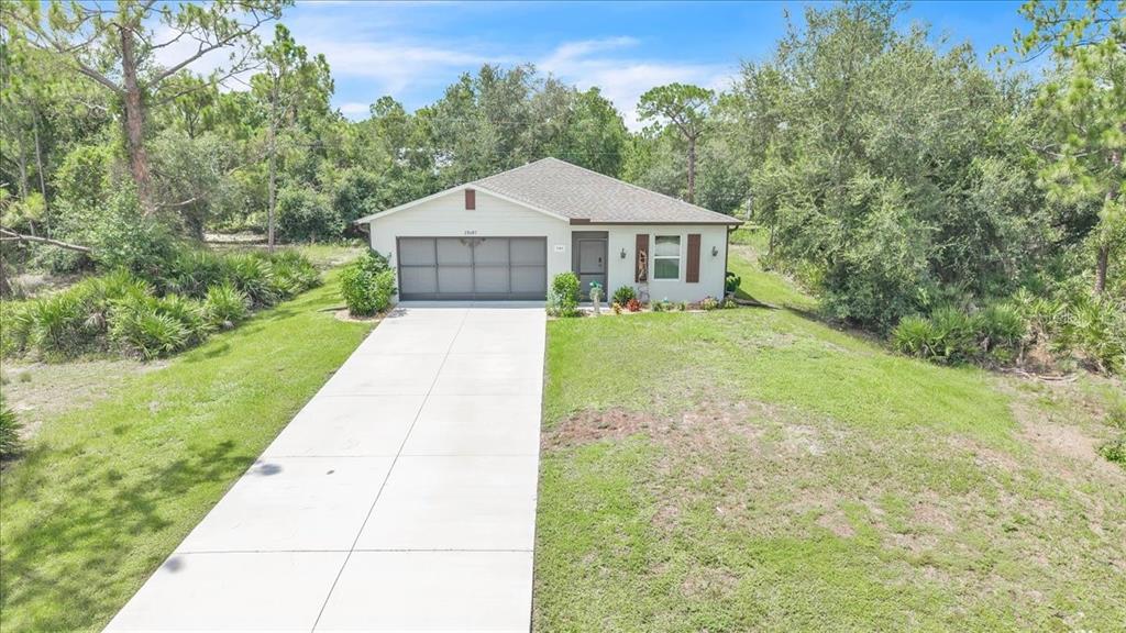 A single-story house with a two-car garage and a concrete driveway surrounded by trees — 28087 CHINQUAPIN DRIVE, PUNTA GORDA, FL