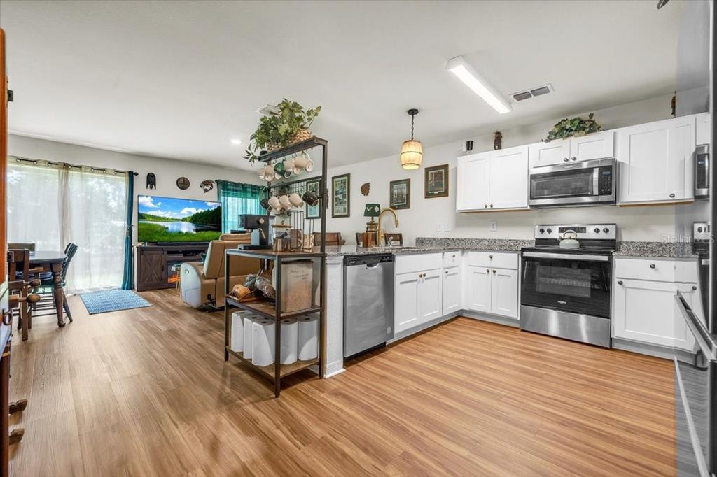 An open-concept kitchen with white cabinets, stainless steel appliances, and wood-look flooring — 28087 CHINQUAPIN DRIVE, PUNTA GORDA, FL