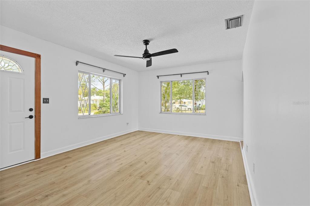 An empty living room features light wood-look flooring, white walls, and two windows — 6206 S FOSTER AVENUE, TAMPA, FL