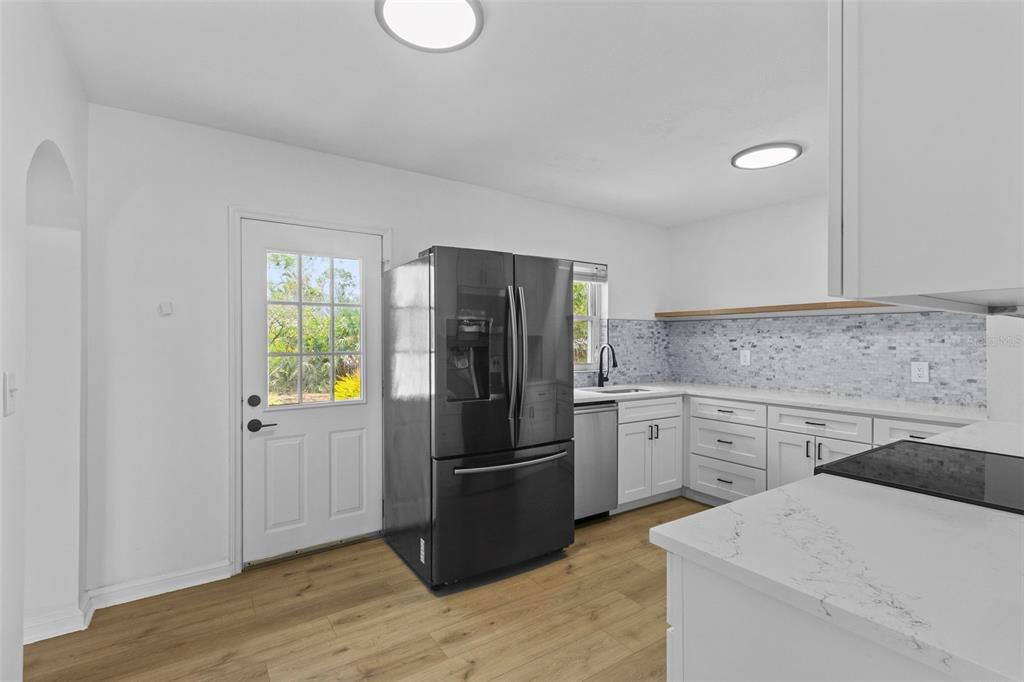 A kitchen with white cabinets, a dark refrigerator, light wood flooring, and a tiled backsplash — 6206 S FOSTER AVENUE, TAMPA, FL
