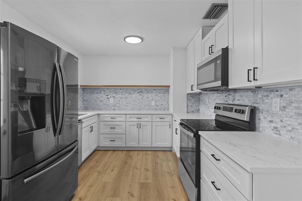 A kitchen features white cabinets, stainless steel appliances, a mosaic backsplash, and light wood flooring — 6206 S FOSTER AVENUE, TAMPA, FL