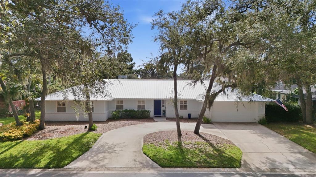 A single-story house with a white metal roof, blue front door, and a circular driveway — 5505 BENEVA WOODS CIRCLE, SARASOTA, FL