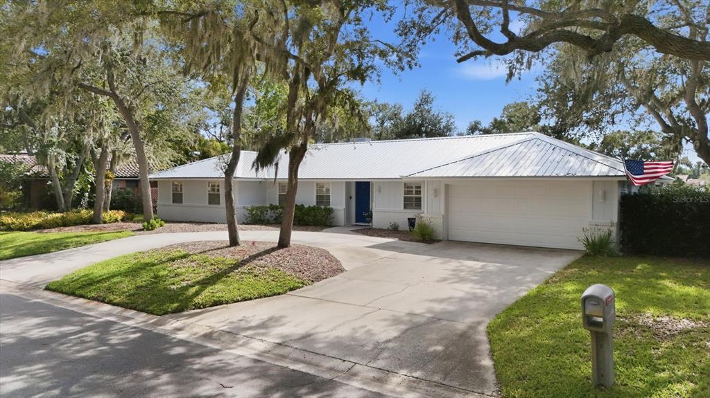 A single-story house with a white metal roof, a two-car garage, and a circular driveway — 5505 BENEVA WOODS CIRCLE, SARASOTA, FL