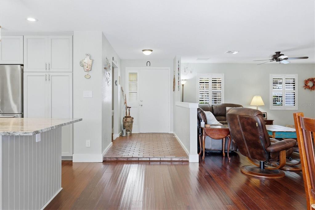 A kitchen island and living area feature hardwood floors, a tiled entryway, and white cabinetry — 5505 BENEVA WOODS CIRCLE, SARASOTA, FL