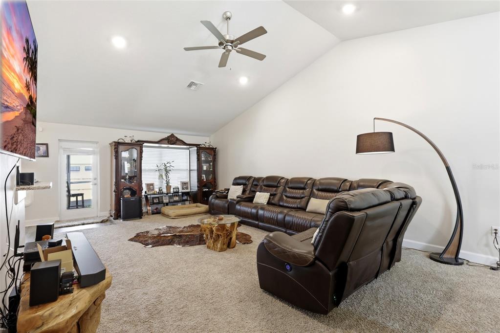 A living room features a large brown sectional sofa, a ceiling fan, and carpeted flooring — 5513 MYRTLE DRIVE, FORT PIERCE, FL
