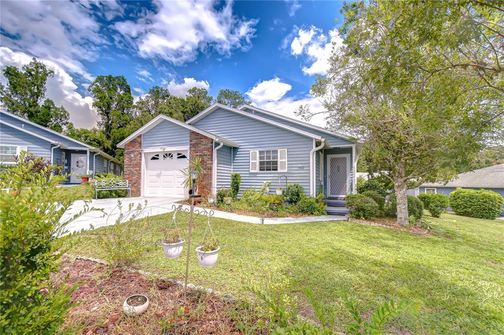 A blue single-story house with a brick-accented garage and a front lawn with landscaping — 5912 NEWBERRY COURT, ZEPHYRHILLS, FL