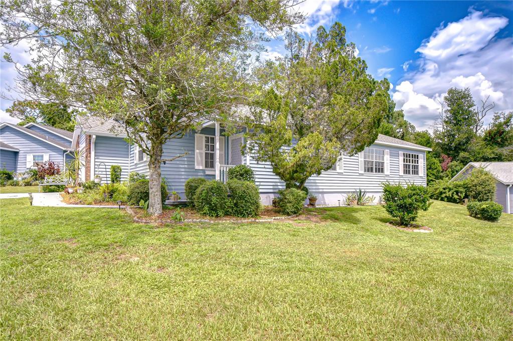 A light blue, single-story house with white shutters sits behind a large tree and lawn — 5912 NEWBERRY COURT, ZEPHYRHILLS, FL