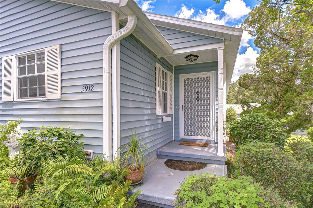 The exterior of a blue-sided house features a covered front porch and a screen door — 5912 NEWBERRY COURT, ZEPHYRHILLS, FL