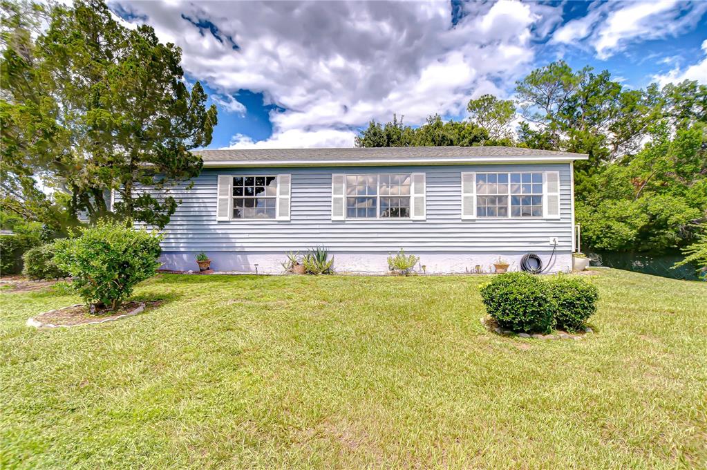 The exterior of a light blue single-story house features three windows and a grassy yard — 5912 NEWBERRY COURT, ZEPHYRHILLS, FL