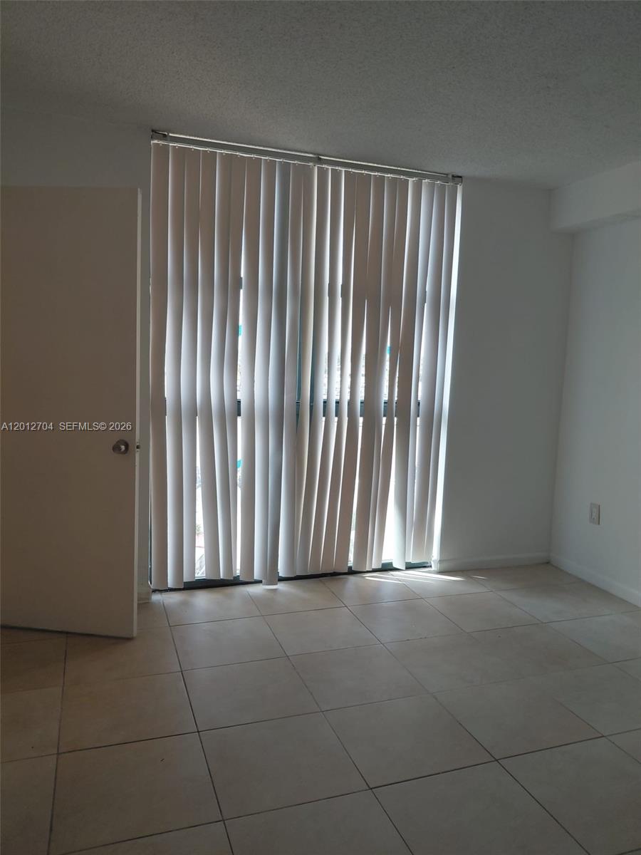 A room with light-colored tile flooring and vertical blinds covering a sliding glass door — 11790 SW 18th St # 3, Miami FL 33175, MIAMI, FL