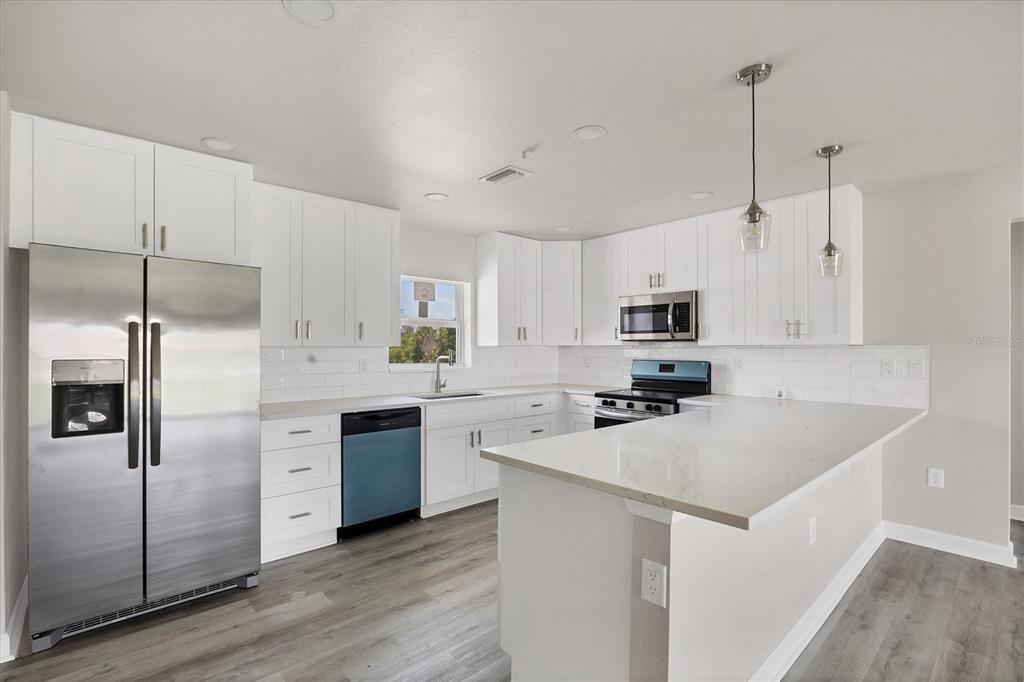 A modern kitchen features white cabinetry, stainless steel appliances, a peninsula, and light-colored countertops — 234 BOUNDARY BOULEVARD, ROTONDA WEST, FL