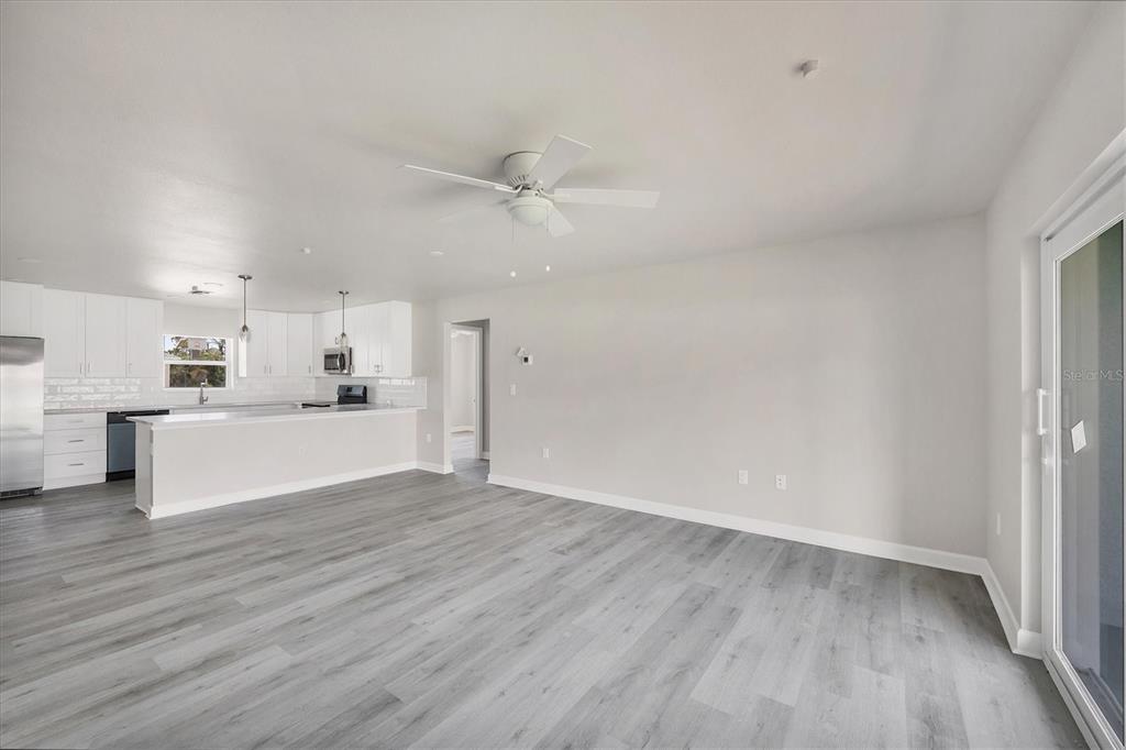 An open-concept kitchen and living area feature white cabinetry, stainless steel appliances, and gray flooring — 234 BOUNDARY BOULEVARD, ROTONDA WEST, FL