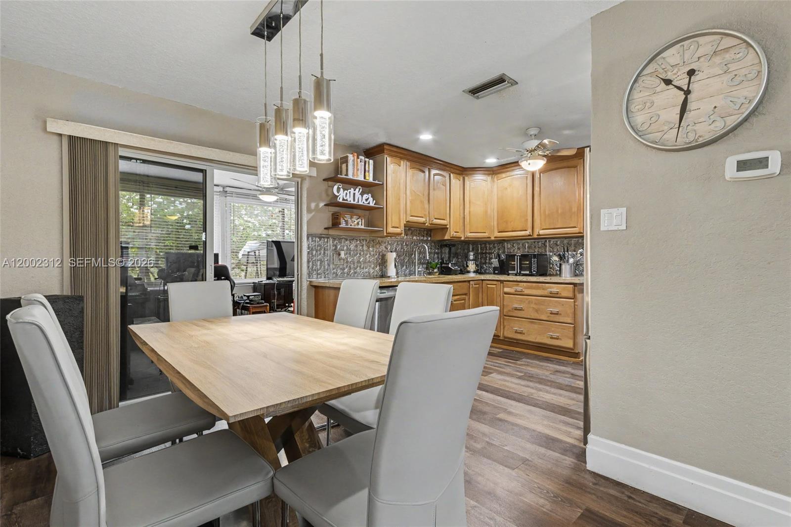 A dining area with a wooden table and chairs sits adjacent to a wood-cabinet kitchen — 4871 NW 13th Ave, Deerfield Beach FL 33064, DEERFIELD BEACH, FL