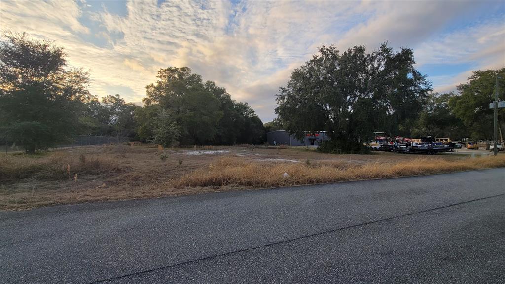 A vacant, grassy lot sits alongside an asphalt road with trees and a building nearby — NW 246 STREET, HIGH SPRINGS, FL
