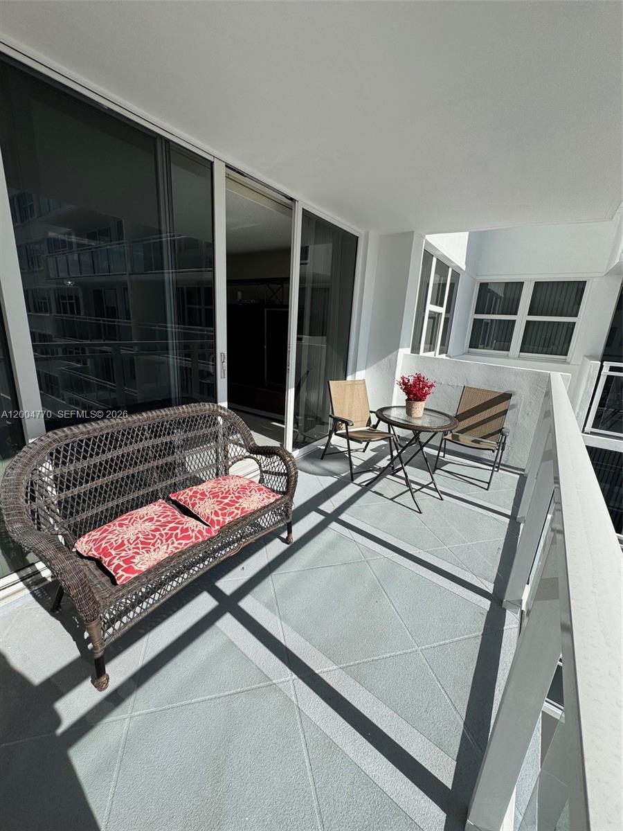 A balcony features a wicker loveseat, a small round table with two chairs, and tile flooring — 2030 S Ocean Dr # 403, Hallandale Beach FL 33009, HALLANDALE BEACH, FL