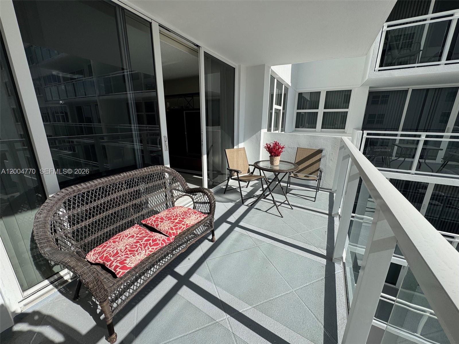 A balcony features a wicker bench with red cushions, a small table, and two chairs — 2030 S Ocean Dr # 403, Hallandale Beach FL 33009, HALLANDALE BEACH, FL