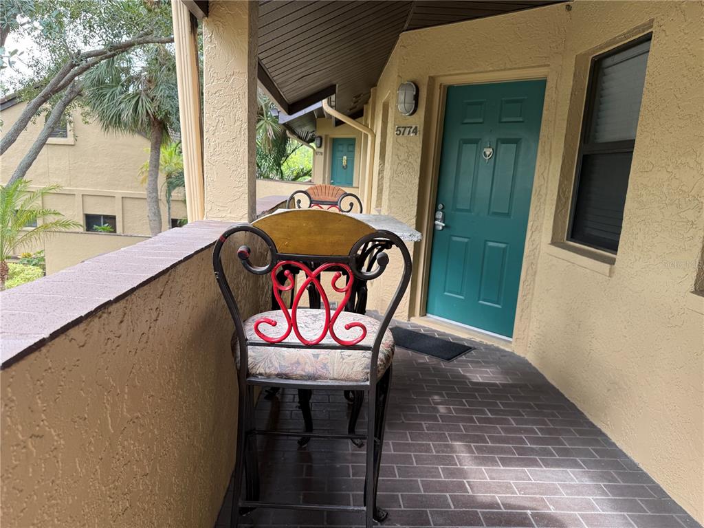 A balcony features a bistro set with metal chairs and a teal door — 5770 ASHTON LAKE DRIVE UNIT 8, SARASOTA, FL