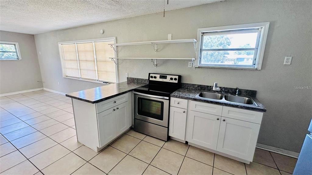 A kitchen features white cabinets, a stainless steel stove, a double sink, and tiled floors — 1310 N COMBEE ROAD UNIT 7, LAKELAND, FL