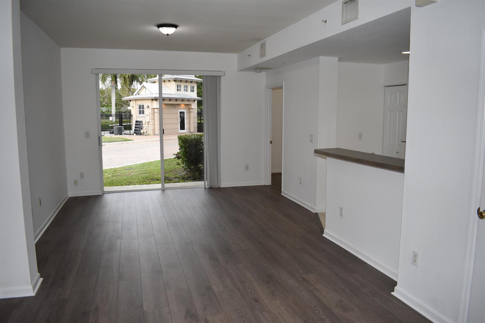 An empty living room with wood-look flooring, a breakfast bar, and a sliding glass door — 1954 Marsh Harbor Drive # 101, Riviera Beach FL 33404, RIVIERA BEACH, FL