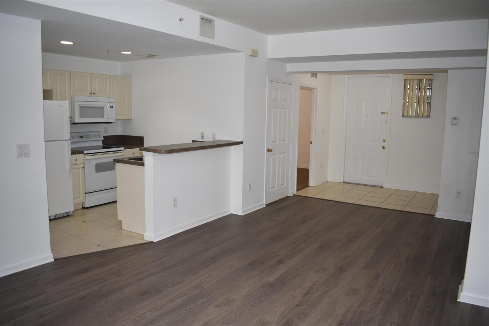 An open-concept apartment featuring a kitchen with white appliances, a breakfast bar, and wood flooring — 1954 Marsh Harbor Drive # 101, Riviera Beach FL 33404, RIVIERA BEACH, FL