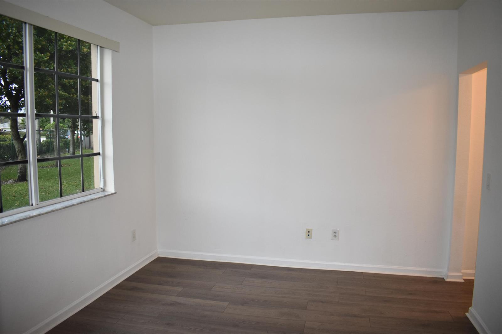 An empty room with white walls, dark wood-look flooring, and a window overlooking a yard — 1954 Marsh Harbor Drive # 101, Riviera Beach FL 33404, RIVIERA BEACH, FL