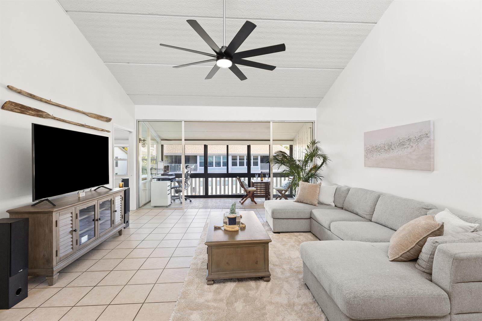 A living room features a gray sectional, wooden coffee table, tile floors, and a ceiling fan — 1456 NE Ocean Boulevard # 202, Stuart FL 34996, STUART, FL