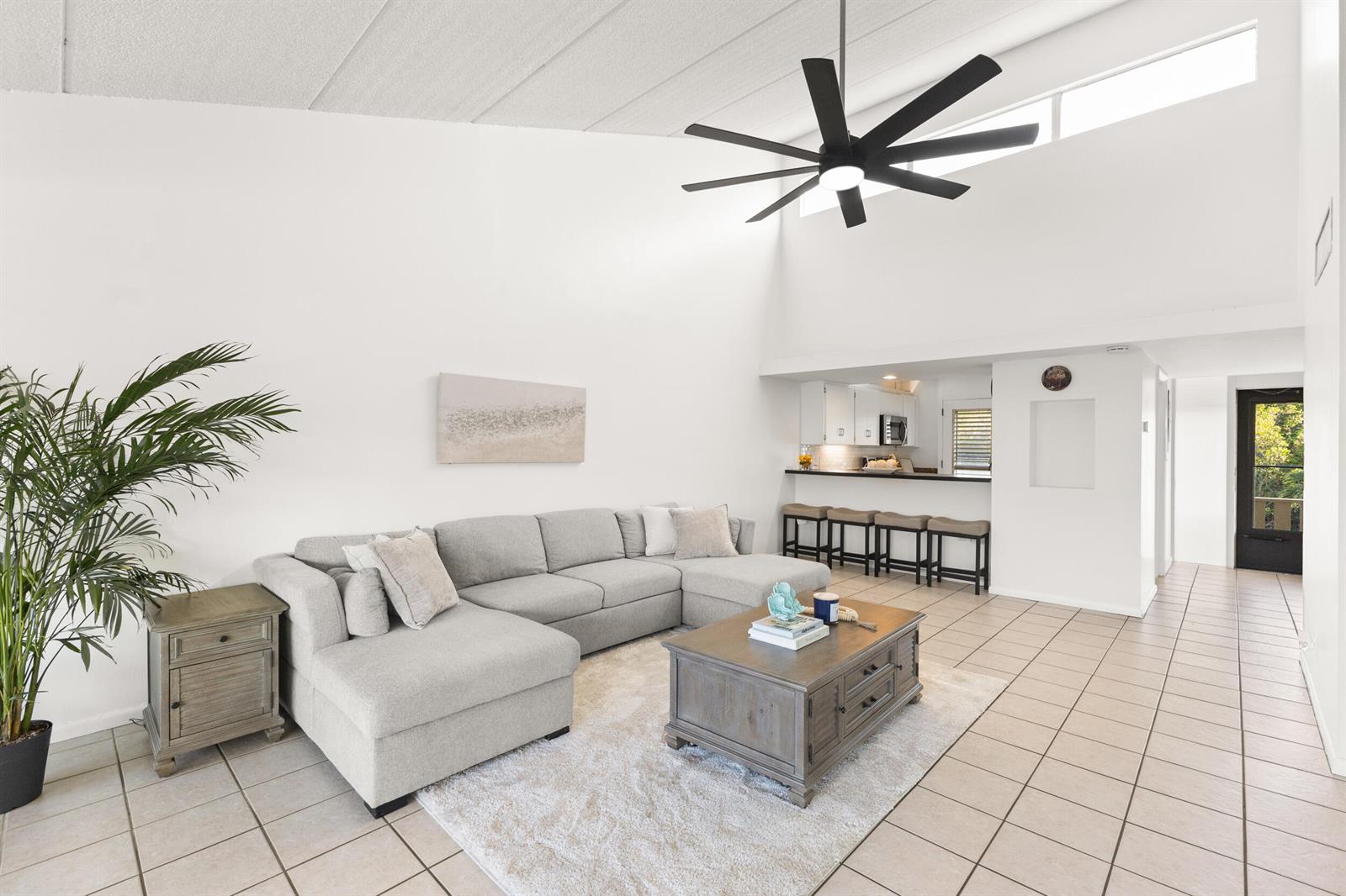 A living room with a sectional sofa, coffee table, and ceiling fan opens to a kitchen — 1456 NE Ocean Boulevard # 202, Stuart FL 34996, STUART, FL