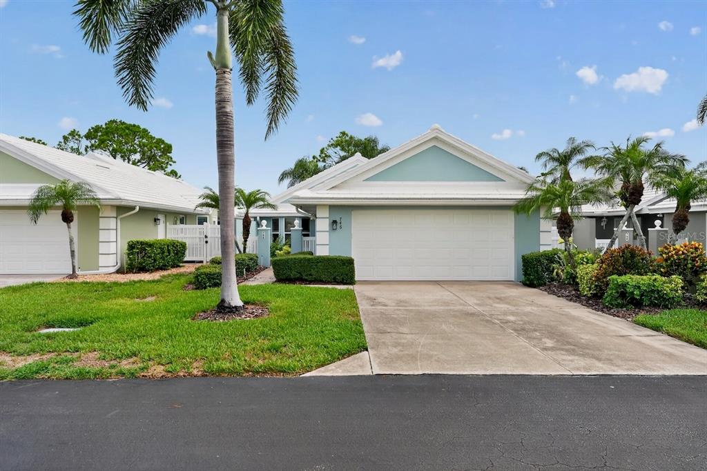 A light blue single-story house with a white garage door and palm trees — 746 HARRINGTON LAKE DRIVE N UNIT 117, VENICE, FL